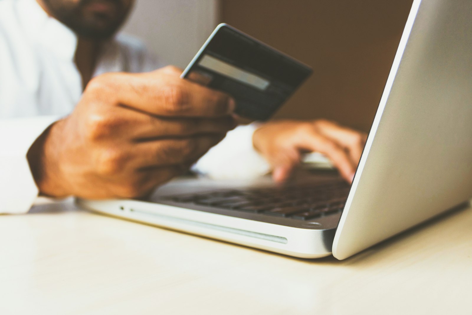 A person holding a payment card beside a laptop